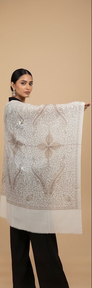 Woman holding a large white and gray patterned shawl against a beige background