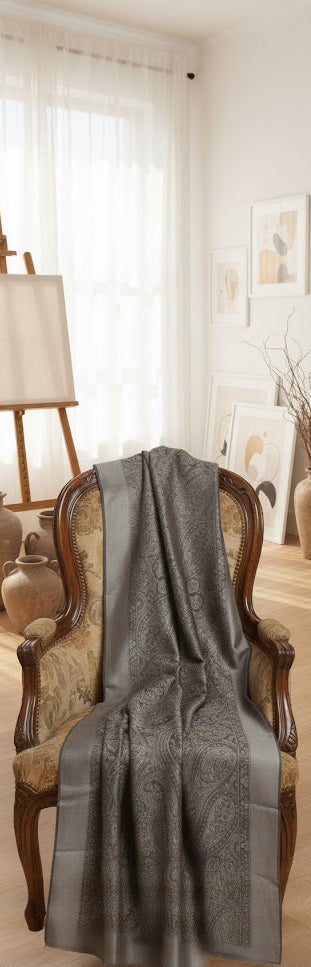 Gray textured shawl draped over a wooden chair in a room with a lamp and window.