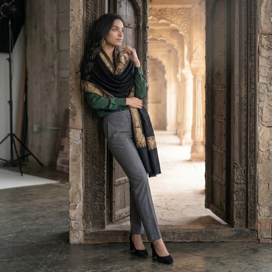 A woman posing in a carved stone corridor, wearing a green long-sleeve top, grey trousers, and a black and gold patterned scarf.