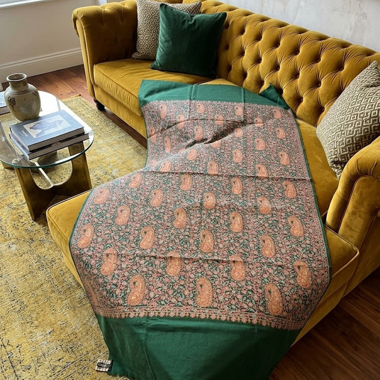 A green and beige patterned shawl or scarf draped over a mustard yellow tufted sofa in a living room setting.