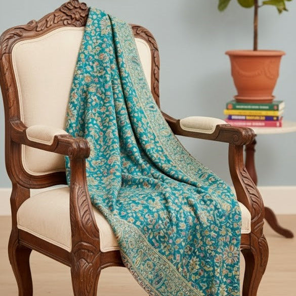 Teal floral shawl draped over a wooden chair with a plant and books in the background.