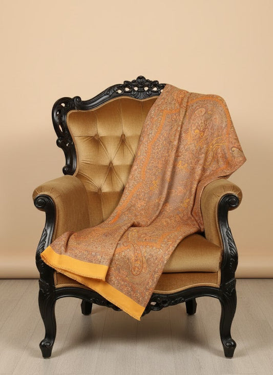Decorative saffron gold yellow pure wool hand embroidered kani jamawar shawl with intricate patterns draped over an ornate chair against a beige background