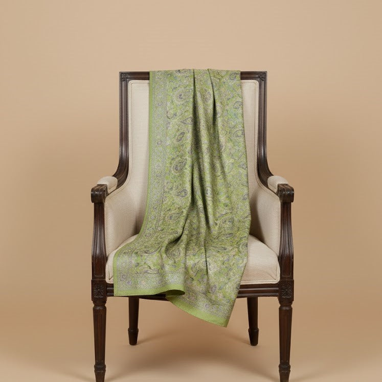 Sage green paisley patterned faux pashmina silk blend draped over a white chair against a beige background