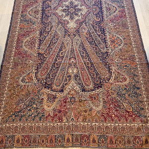 A long, ornate Persian-style area rug with a central medallion and intricate floral motifs, laid out on a light-colored wooden floor in a room.