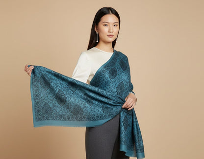 Female Model holding a blue patterned faux Pashmina stole against a beige background