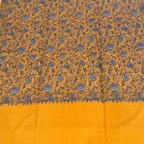 A close-up of a mustard yellow fabric with an intricate blue and brown floral block print pattern and a solid mustard yellow border.