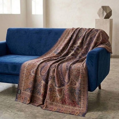 A patterned throw blanket draped over a blue velvet sofa in a modern, sunlit room with textured walls and concrete floors.