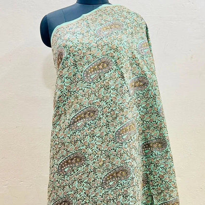 A sage green and brown paisley printed shawl draped on a black mannequin torso against a light beige wall.