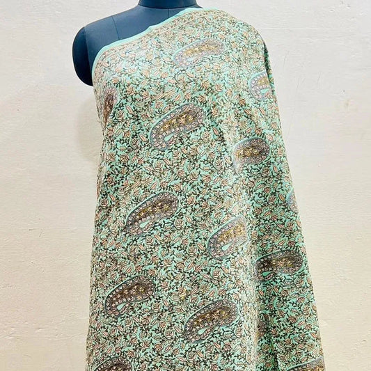 A sage green and brown paisley printed shawl draped on a black mannequin torso against a light beige wall.