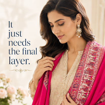 A woman wearing a traditional outfit with a bright pink dupatta featuring intricate red and beige patterns, layered over a cream-colored embroidered kurta. Text on the left reads, 'It just needs the final layer.