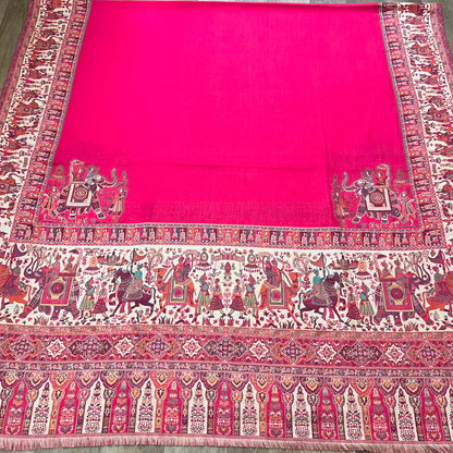 A vibrant pink kalamkari shawl laid flat on a wooden floor, featuring a solid pink center field and ornate traditional borders with detailed motifs.