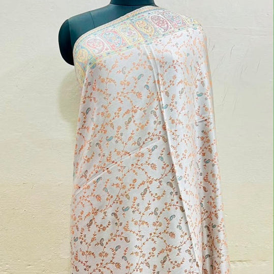 A light pink and white printed saree draped on a black mannequin torso against a beige wall. The fabric features delicate floral patterns in pink, orange, and green, with a decorative border along the edge.