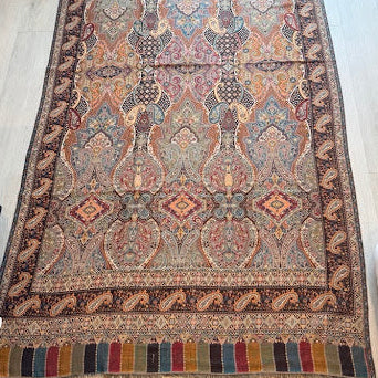 A rectangular traditional area rug with an intricate multicolor floral and geometric pattern, laid out on a light wood floor.