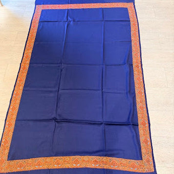 A royal blue fabric runner or scarf with a decorative orange border, laid flat on a light-colored wooden floor.