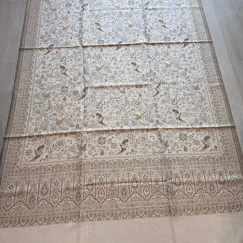 A large beige and brown patterned rug laid flat on a light wood floor, featuring intricate traditional motifs and a wide decorative border.