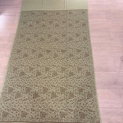 An olive green woven runner or scarf with an intricate beige and brown paisley pattern, laid flat on a light-colored wooden floor.