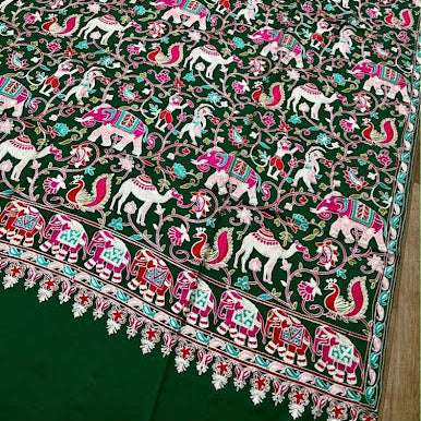 A dark green area rug with an intricate hand-embroidered pattern of white elephants, pink peacocks, and floral motifs, finished with a decorative border and tassel fringe.