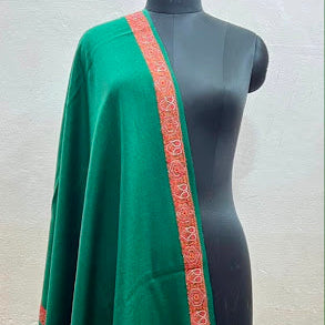 A green shawl with a rust-orange patterned border draped over a black mannequin torso against a light gray wall.