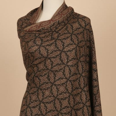 A dark black shawl with a geometric floral pattern and striped border, displayed on a mannequin torso against a solid beige background.