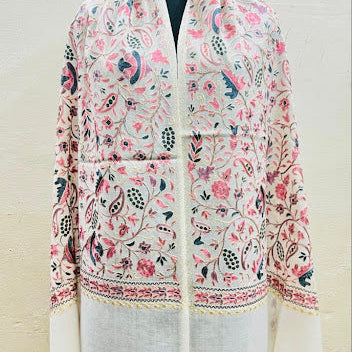 A cream-colored shawl jacket with intricate pink, green, and blue floral and paisley embroidery, displayed on a black mannequin torso against a light beige wall.