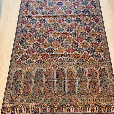 A long, narrow Persian-style area rug with an intricate geometric and floral pattern in red, blue, beige, and brown, laid out on a light wood floor.