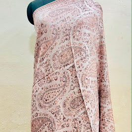A draped fabric with a dusty pink and brown paisley pattern, displayed on a black dress form mannequin against a textured beige wall.