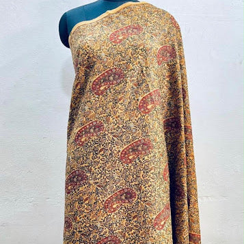 A draped patterned fabric, likely a sari, displayed on a dark teal mannequin torso against a white wall. The fabric features a dense, intricate paisley and floral print in shades of brown, gold, and rust red.
