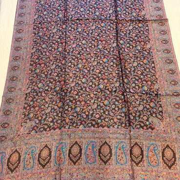 A long rectangular area rug laid flat on a light wood floor, featuring an intricate floral pattern in a dark brown base with pink, blue, and orange accents, and a decorative border with paisley motifs.