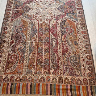 A rectangular traditional area rug with an intricate multicolor paisley and floral pattern, laid out on a light-colored wooden floor in a room.