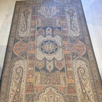 An ornate rectangular area rug with a traditional Persian-style medallion and paisley pattern, laid out on a light wood floor next to a sofa.