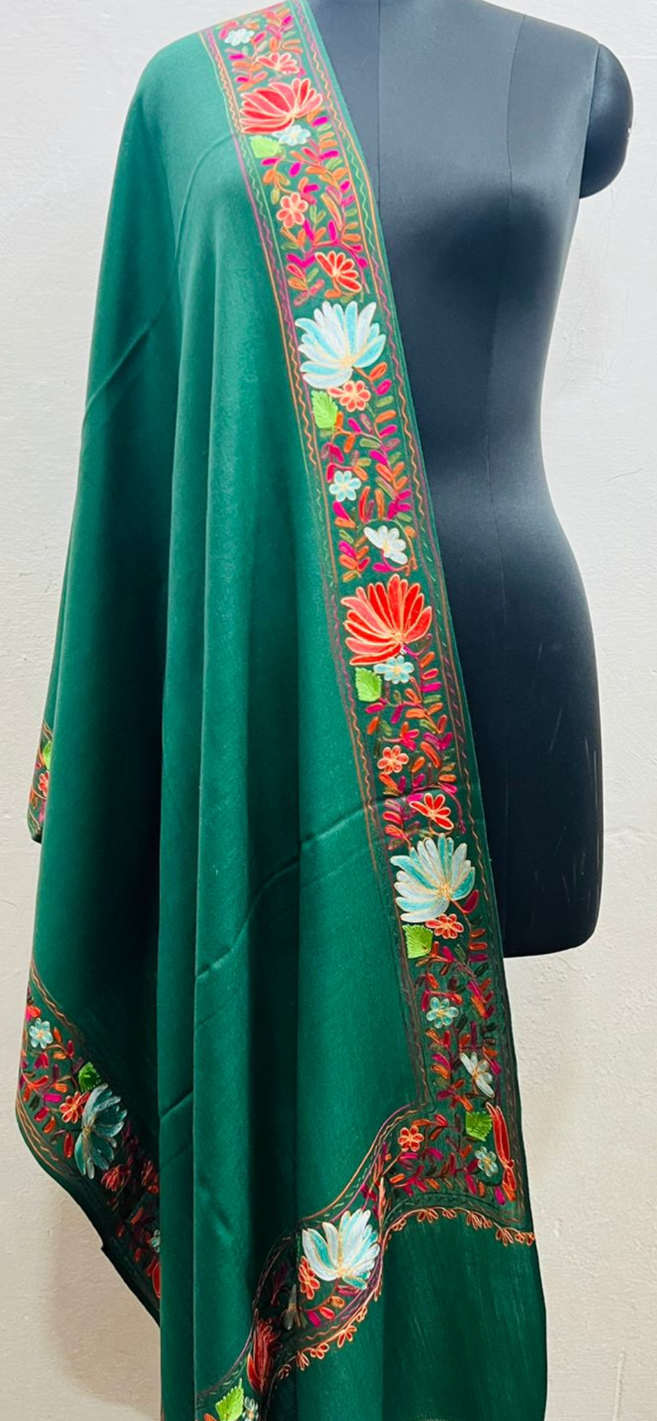Green shawl with colorful floral embroidery on a mannequin against a white background