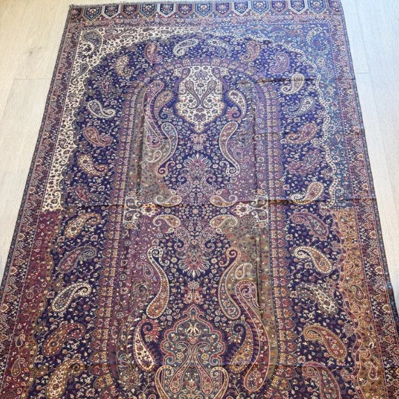 A large traditional oriental area rug with an intricate floral and paisley pattern, displayed on a light wood floor between a sofa and a chair.