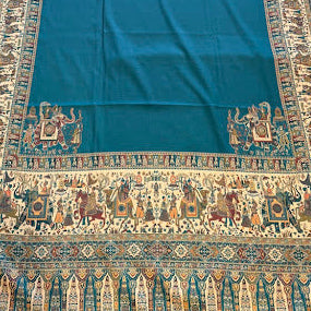 A rectangular teal prayer rug with an ornate traditional border, laid flat on a light wood floor.