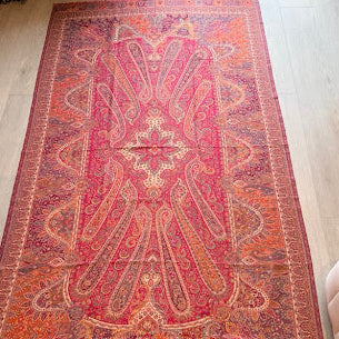 A rectangular Persian-style area rug with an intricate medallion and floral pattern in shades of red, orange, pink, and beige, laid out on a light wood floor in a room.