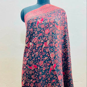 A dark navy blue shawl with a red and pink floral and bird pattern, draped on a black mannequin torso against a plain off-white wall.