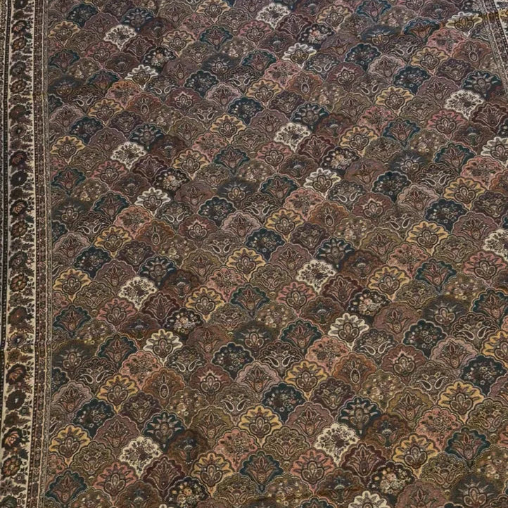 A traditional oriental area rug with an intricate geometric and floral pattern in shades of brown, beige, and muted blue, featuring a decorative border.
