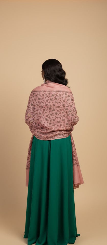 Person wearing a pink floral shawl and green skirt on a beige background