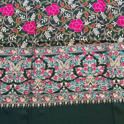 A close-up of a patterned textile with a dark charcoal base, bright pink floral motifs, white leafy vines, and an ornate multicolored border featuring turquoise, pink, beige, and black details.