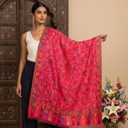Woman holding a vibrant pink and orange patterned scarf with a floral arrangement and decorative vase in the background.