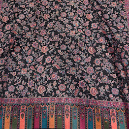 A rectangular black woven runner rug with an all-over pink floral pattern and a colorful striped fringe border, laid flat on a light wood floor.