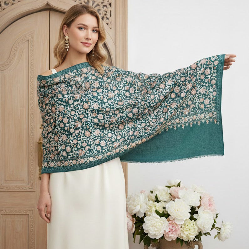 Woman holding a teal floral shawl in front of a wooden door with a vase of flowers on a white background