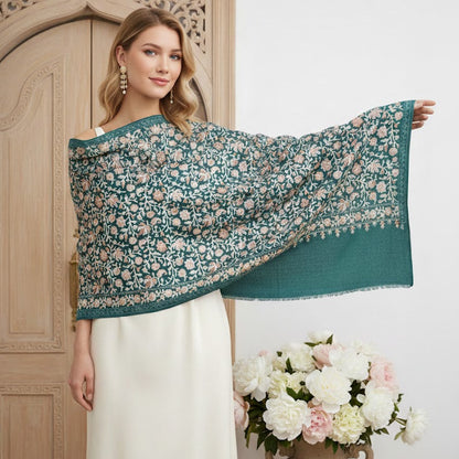 Woman holding a teal floral shawl in front of a wooden door with a vase of flowers on a white background