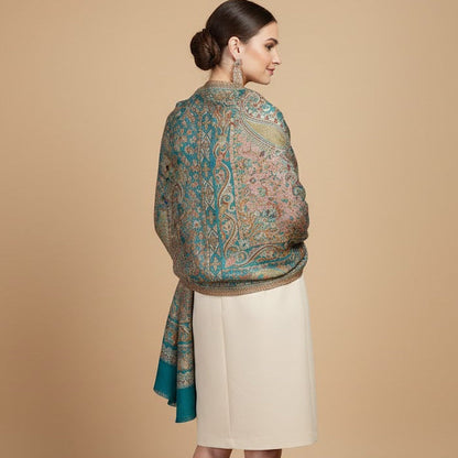 Woman wearing a deep teal blue patterned jamawar kani pure wool shawl over a plain garment on a beige background