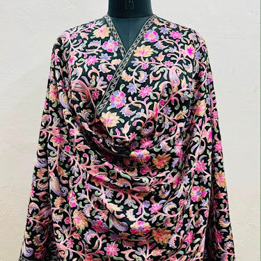A black long-sleeve tunic top with an intricate multicolor floral and paisley pattern, displayed on a black dress form mannequin against a plain off-white wall.