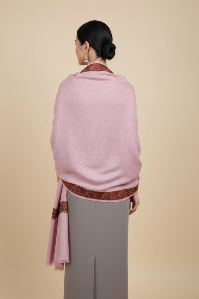 Woman wearing a luxury pashmina kashmiri sozni hand embroidered border dusty pink shawl with a patterned trim on a beige background
