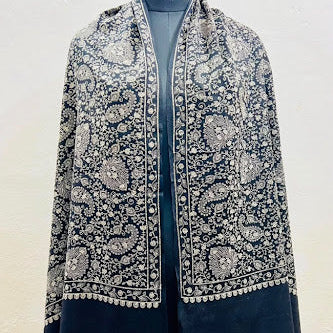 A dark navy blue shawl with intricate silver and white floral embroidery, draped over a black mannequin torso against a plain off-white wall.