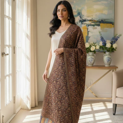 Woman wearing a long, patterned dress standing in a sunlit room with a painting and flowers in the background.