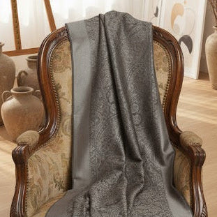 Gray textured shawl draped over a wooden chair in a room with a lamp and window.
