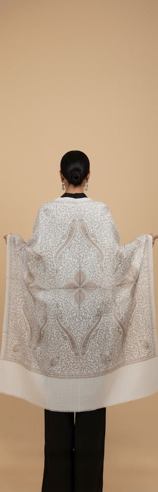 Person wearing a large, patterned shawl over their shoulders against a beige background