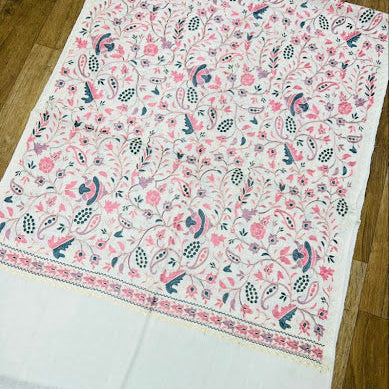 A white fabric textile with an all-over pink and navy floral paisley print, laid flat on a wooden floor.